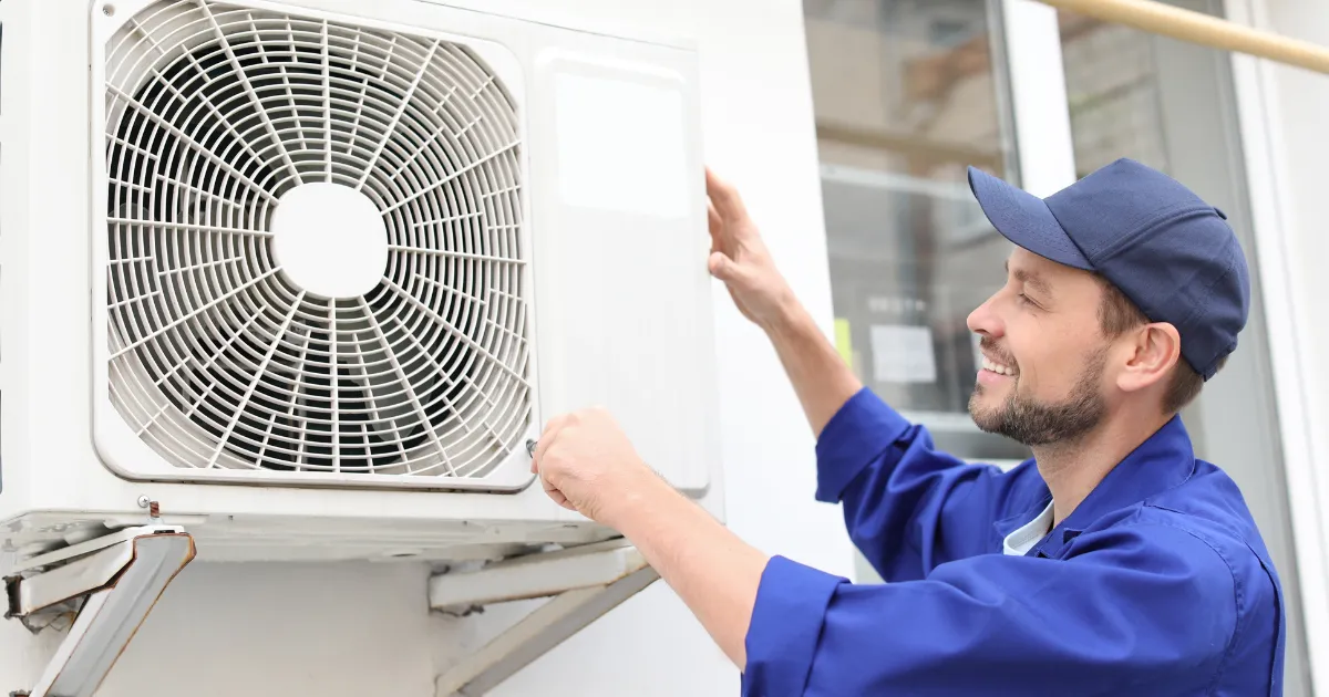 A smiling technician from the Rapid Response Team is adjusting the outdoor AC unit to ensure proper cooling performance