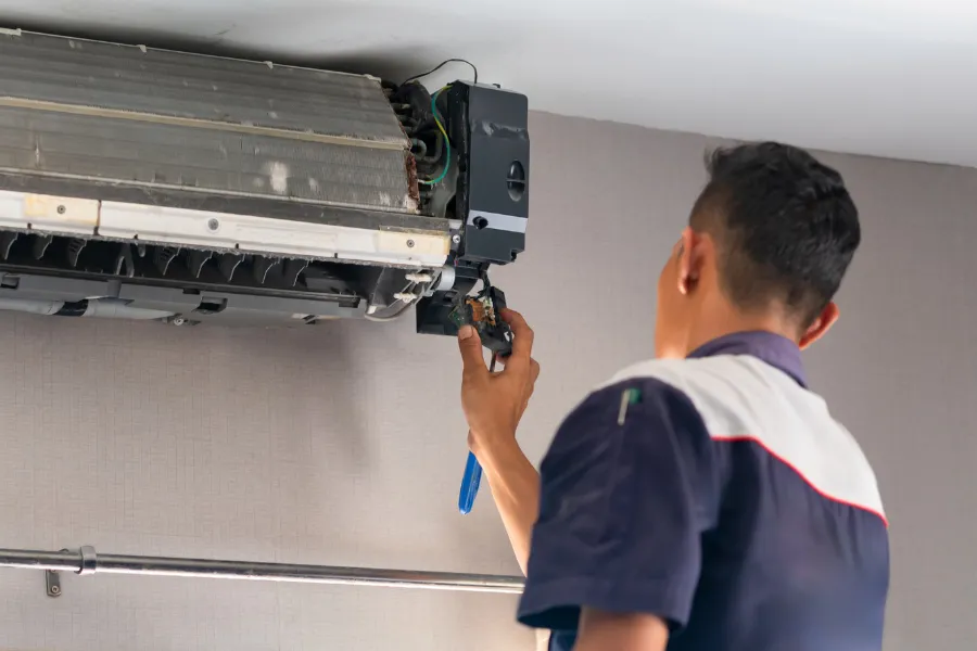 A technician carefully removes a faulty component from a wall-mounted air conditioning unit during a repair service, ensuring proper maintenance and safe operation