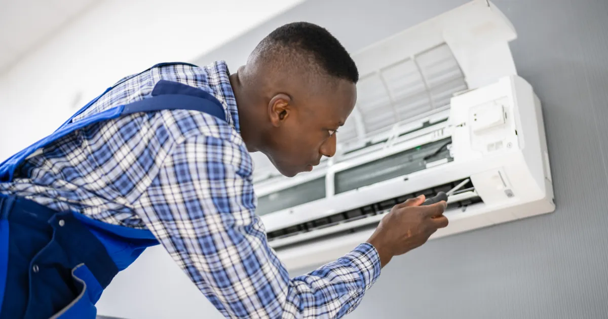A technician in a uniform carefully inspects the internal components of a wall-mounted air conditioning unit 