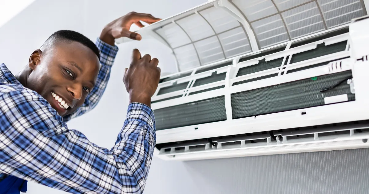 A Rapid Response team member smiling while opening the front cover of a wall-mounted AC unit