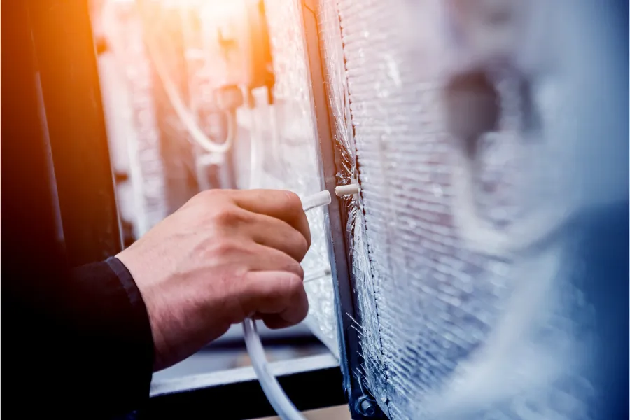 A technician flushing and cleaning an air conditioning drain line to prevent clogs and improve system airflow