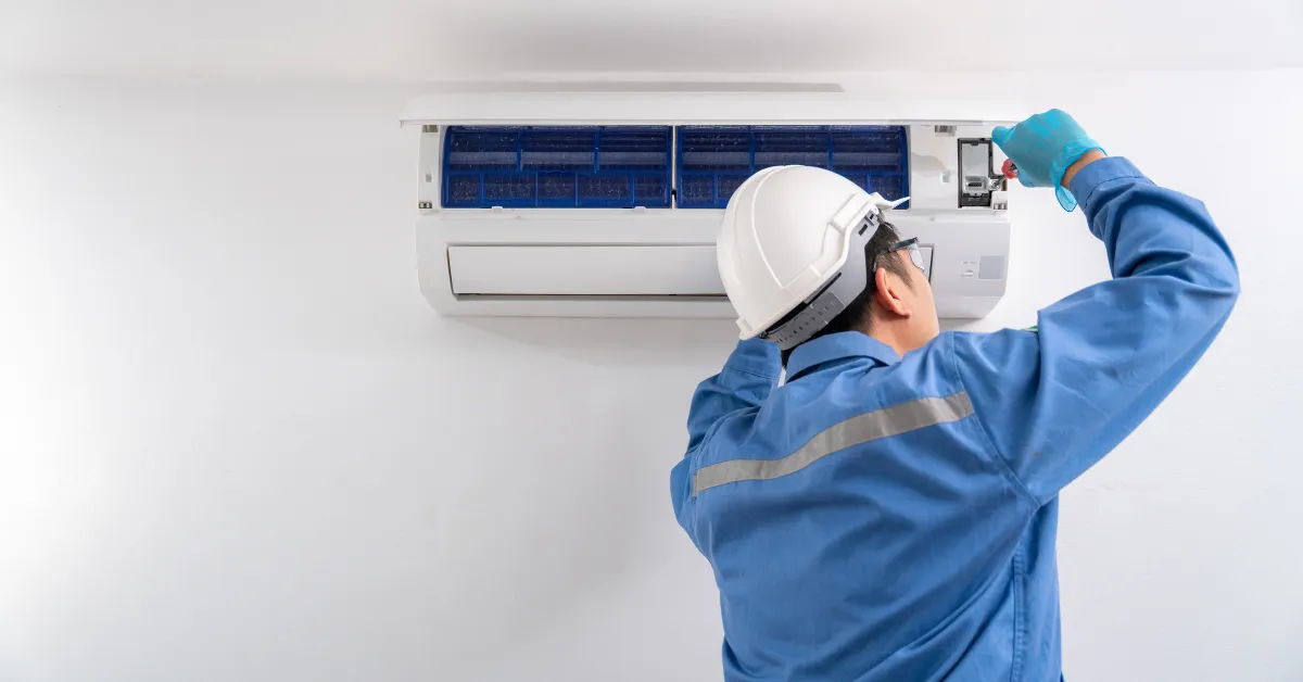 A technician in safety gear inspecting and adjusting a wall mounted air conditioner unit for proper performance