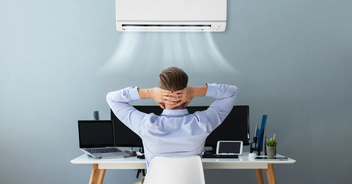 Person relaxing at a desk while cool air flows from a wall-mounted air conditioner, creating a comfortable workspace