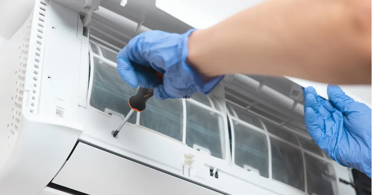 A technician wearing blue gloves is using a screwdriver to remove and clean the air conditioner filter during service