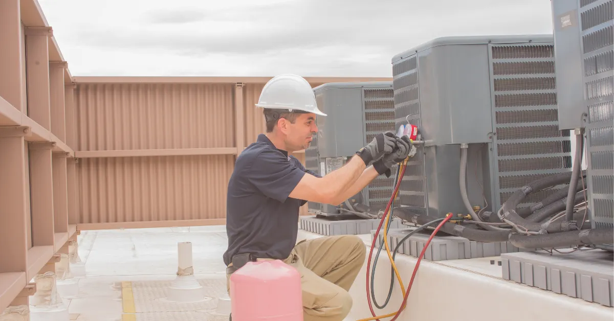 A technician checking a rooftop HVAC unit with gauges and a refrigerant tank during maintenance service