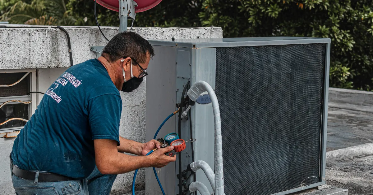 A Rapid Response Team technician wearing a mask checks refrigerant levels on an outdoor AC condenser unit