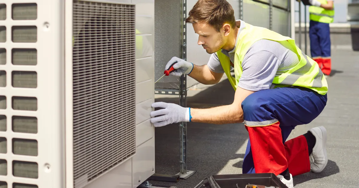 Rapid Response technician in safety gear, tightening the panel on an outdoor AC condenser unit during maintenance service