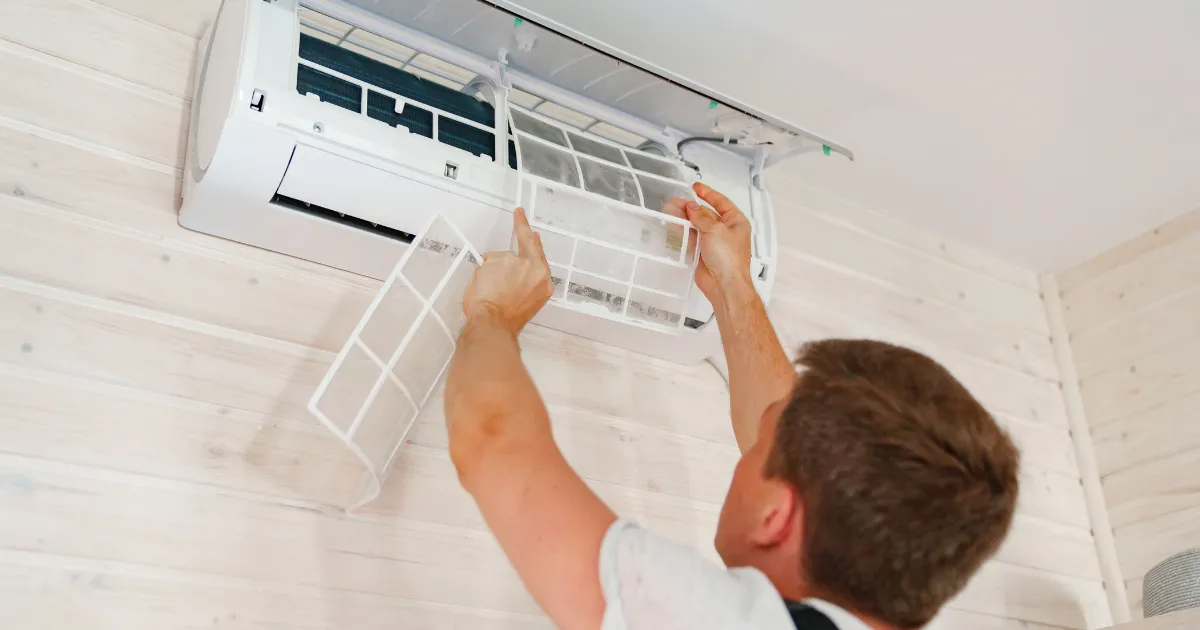A Rapid Response Team member carefully cleans the air filters of a wall-mounted AC unit for better indoor air quality