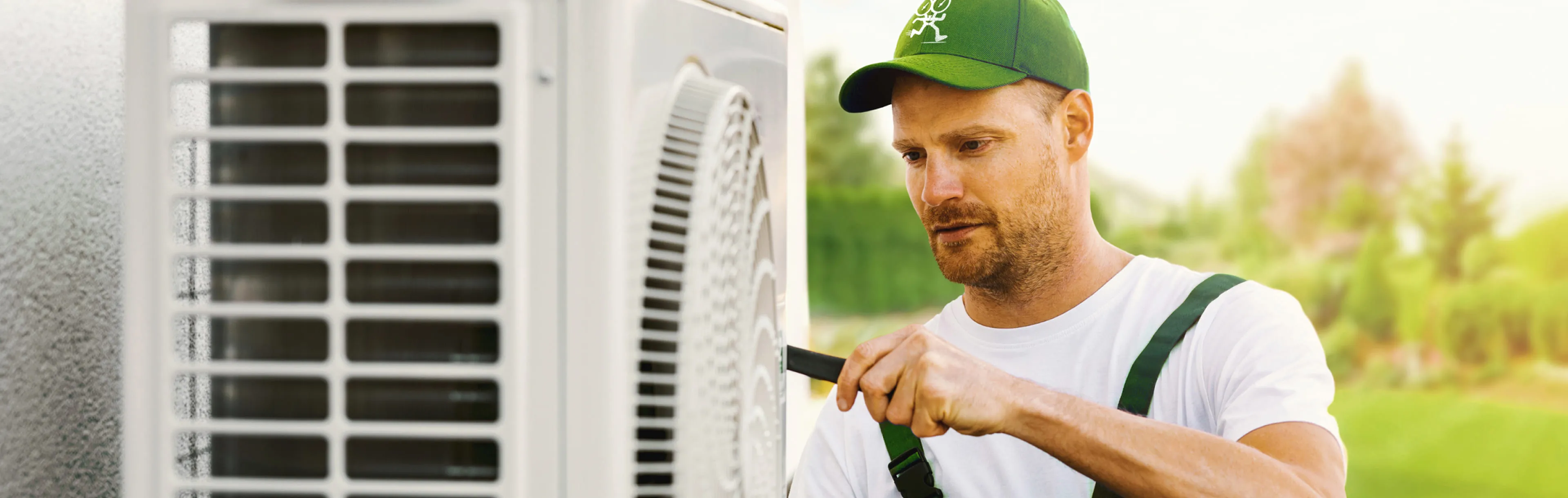 A technician in a green cap tightens the bolts on an outdoor AC condenser during air conditioning installation
