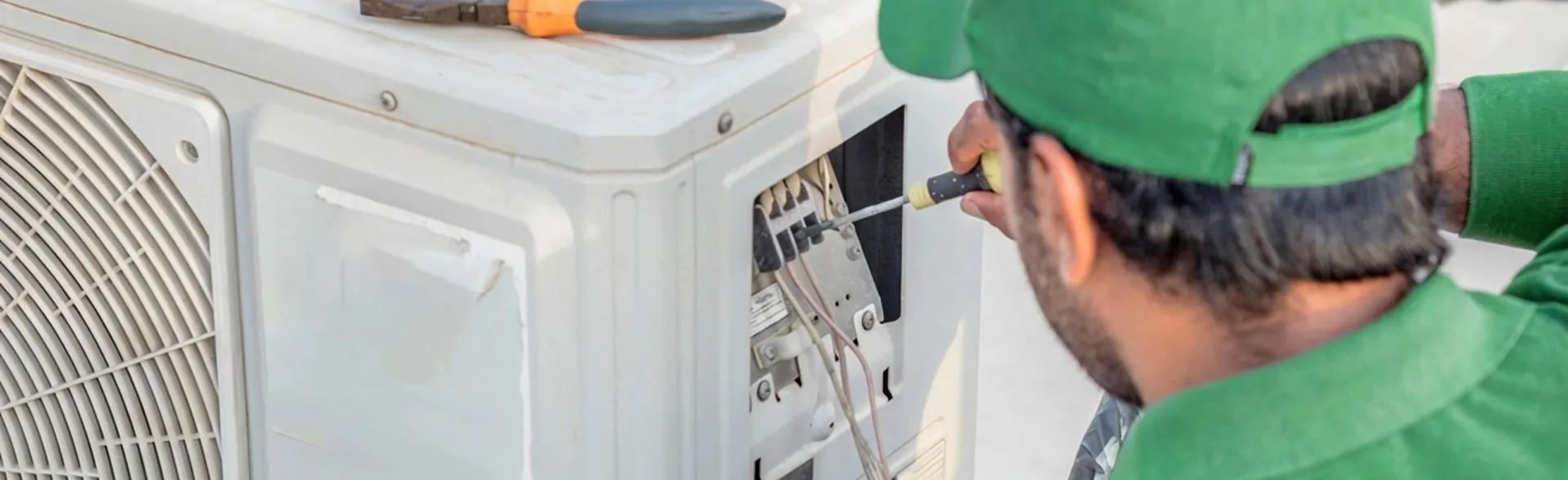 A Rapid Response technician in a green cap tightens the bolts on an outdoor AC condenser during air conditioning installation