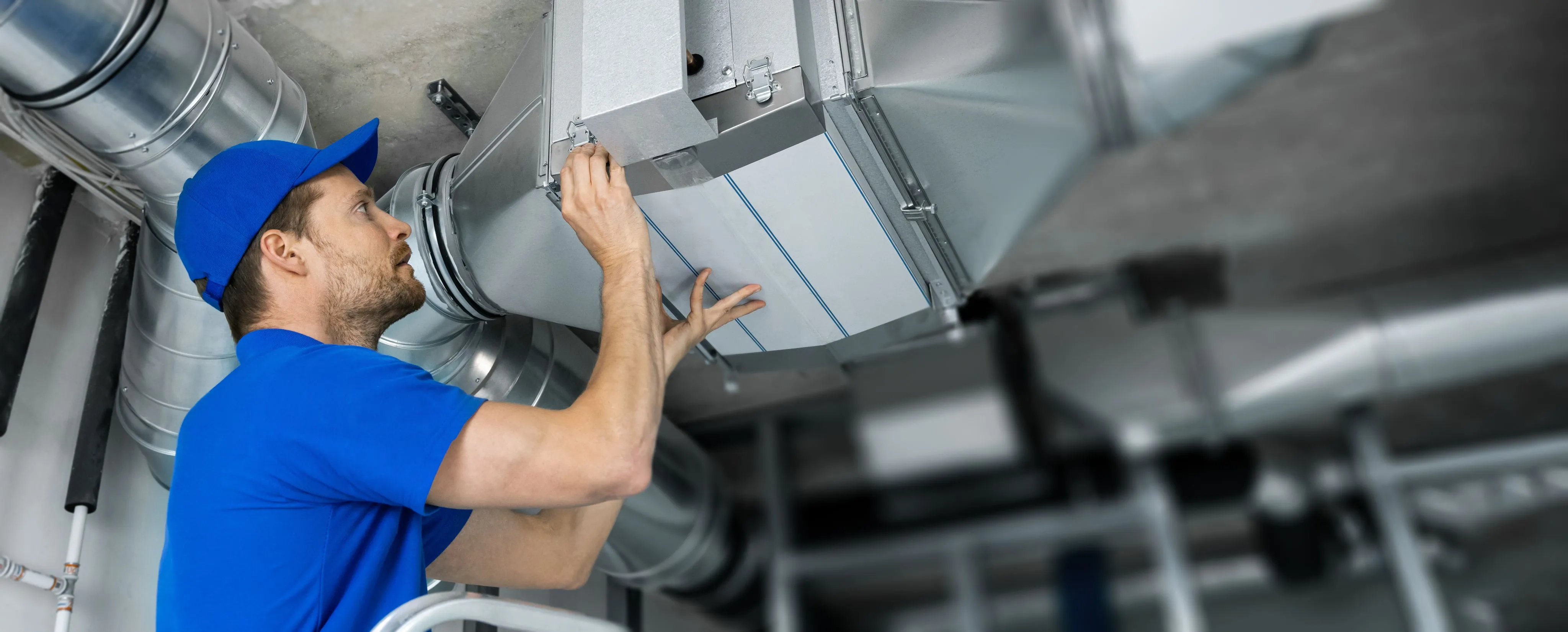 A technician in a green cap tightens the bolts on an outdoor AC condenser during air conditioning installation